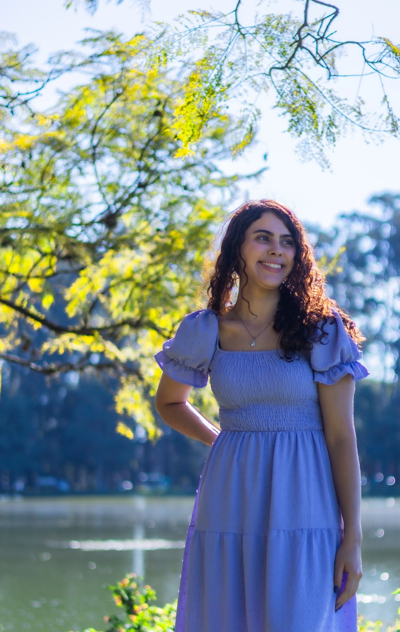 Bia sorrindo com vestido lilás diante do lago