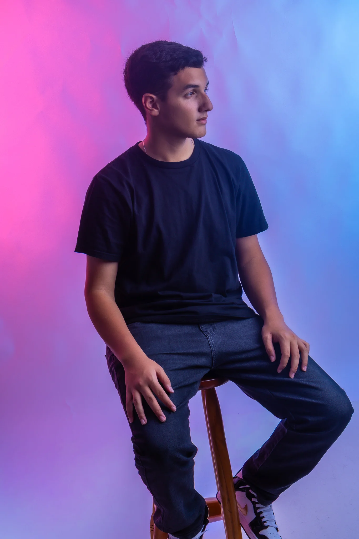 Retrato de corpo inteiro de Vinicius sentado em um banco no estúdio